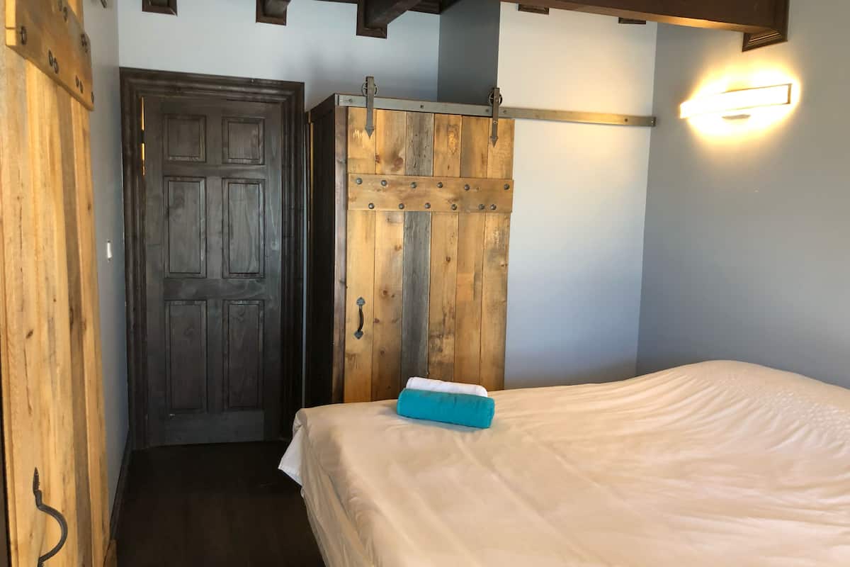 Een slaapkamer met een houten garderobe, een bed met een wit laken en een wandlamp.