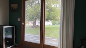 Ein Zimmer mit einer Schiebetür und Zugang zu einem Garten mit Baum und Holzterrasse.