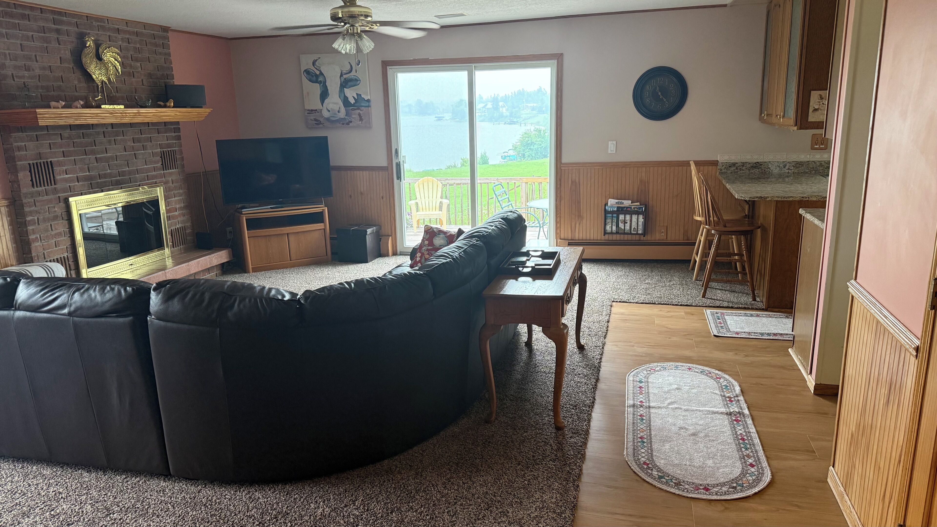 A living room with a sectional sofa, a fireplace, a television, and a view of a lake through large sliding doors.