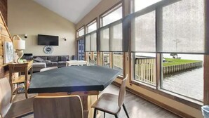 A spacious room with a large dining table, a sofa, and a TV mounted on the wall. - Lovely 2 Bedroom condo with marina view and pool (Seabrook)