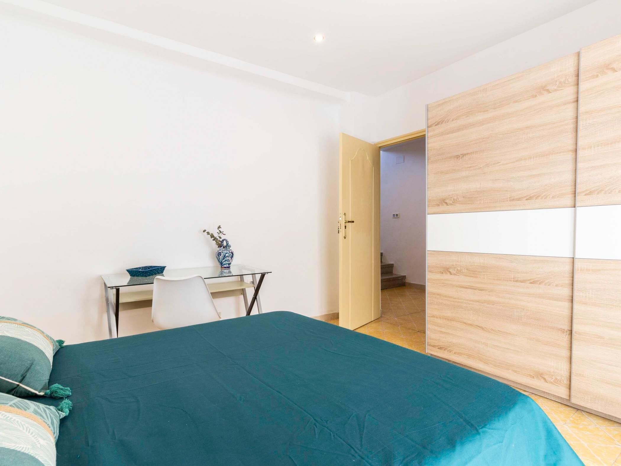 Ein Schlafzimmer mit einem Bett, einem Schreibtisch mit einer Vase und einem Kleiderschrank.