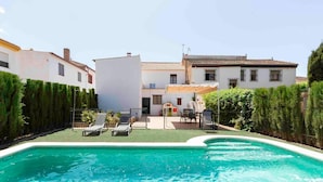 En swimmingpool med liggestole, en overdækket terrasse og en hvid bygning med et tag af fliser.
