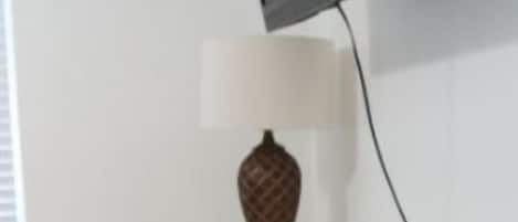 Una habitación con un televisor montado, un aparador blanco, un florero y un objeto decorativo rosa.