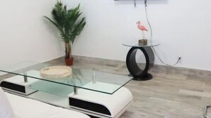 A modern living room with a glass coffee table, white sofa, and a flat-screen TV mounted on the wall. - WoW!! Stunning 1 BR // Prime Singer Island (West Palm Beach)