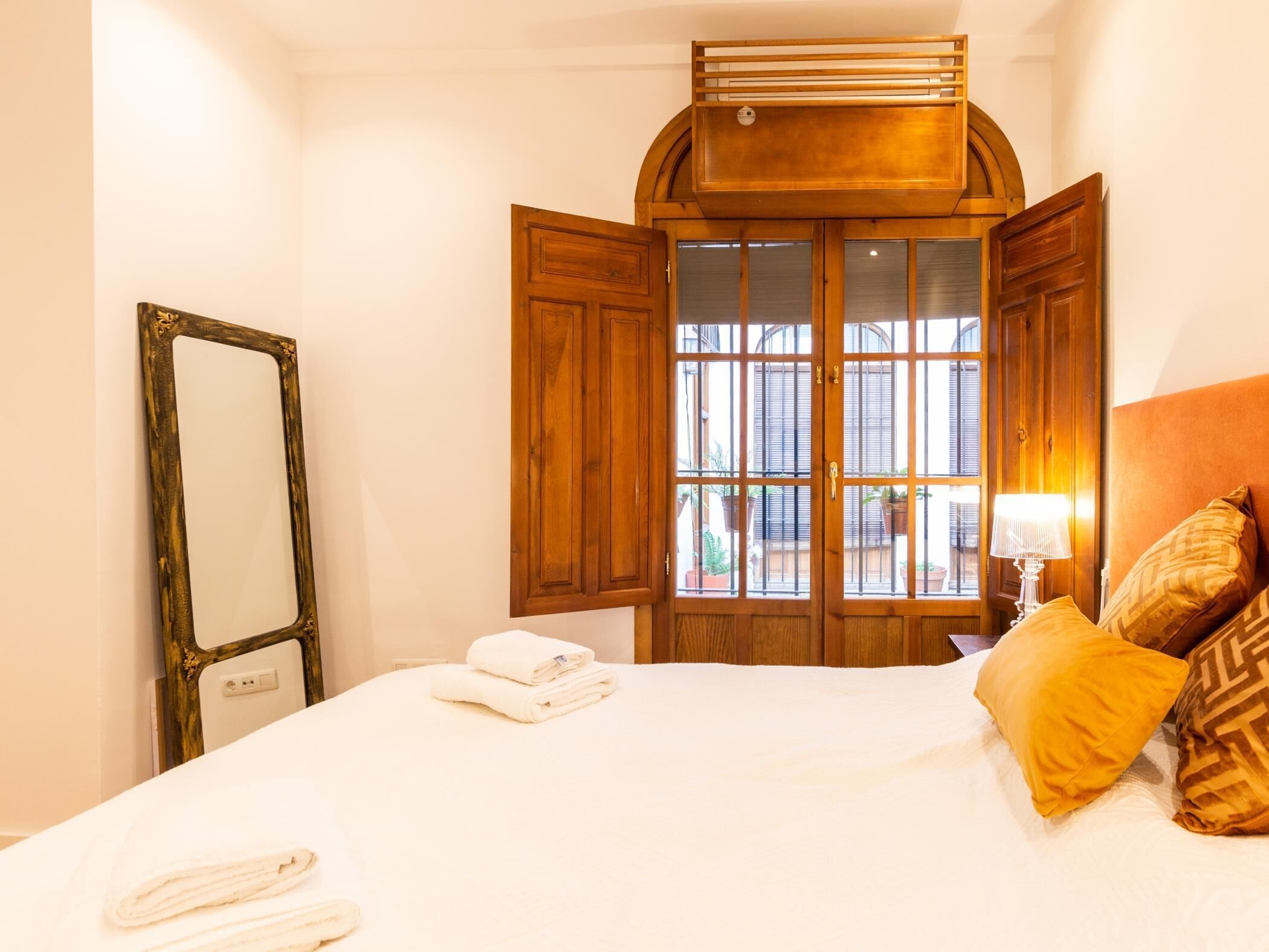 Une chambre d’hôtel avec un grand lit, une armoire en bois, un miroir et une fenêtre dont les volets sont ouverts.