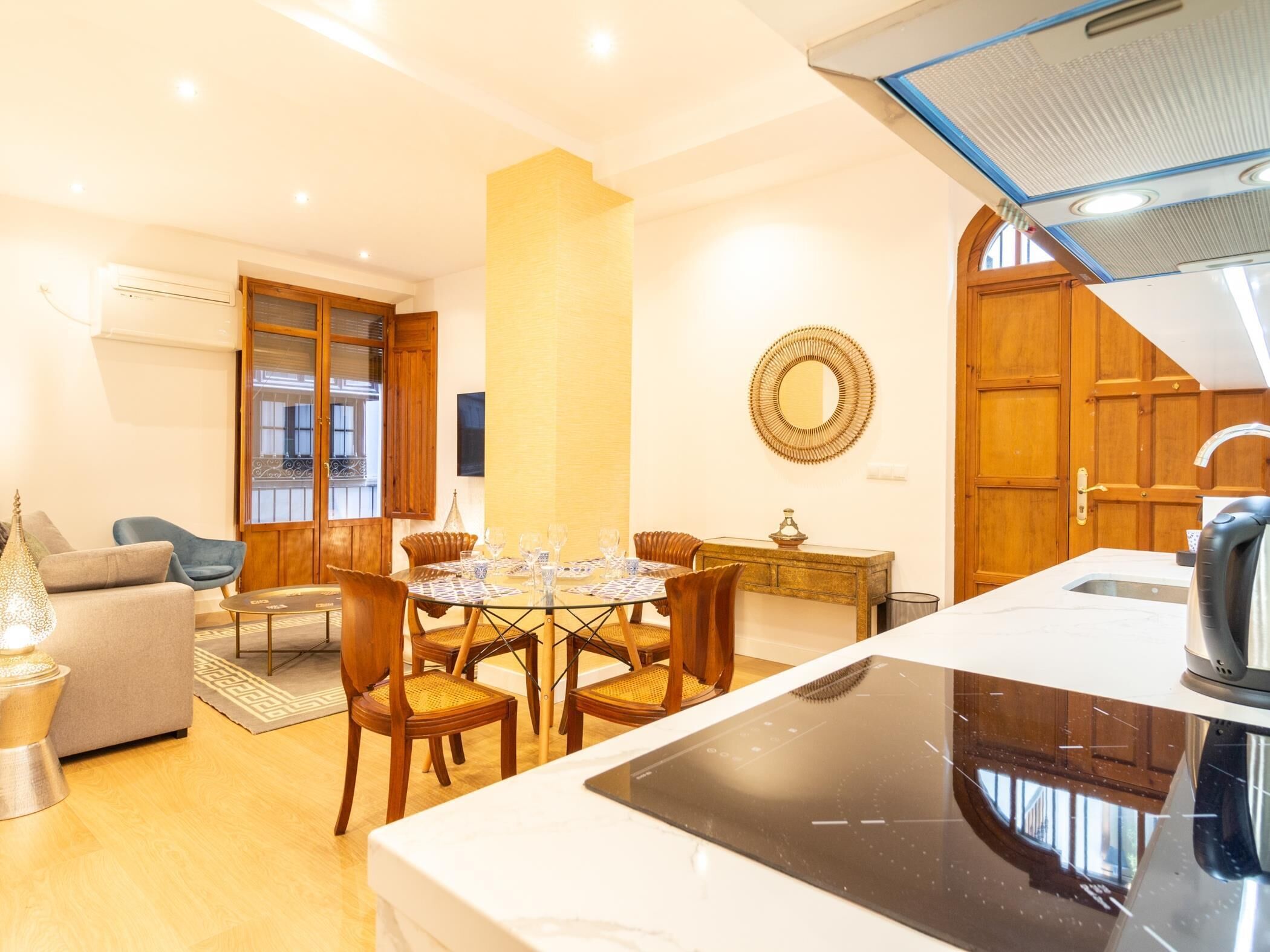 Un salon moderne avec un coin repas, des meubles en bois et une cuisine équipée d’une cuisinière intégrée.