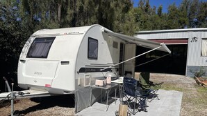 Una caravana blanca con toldo cubierto, una mesa con un tostador y una silla.