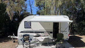 Un vehículo recreativo con zona de comedor cubierta, dos sillas y una mesa.
