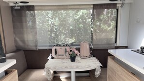 Una cocina compacta con una mesa, tostadora, hervidor y una ventana con persianas.