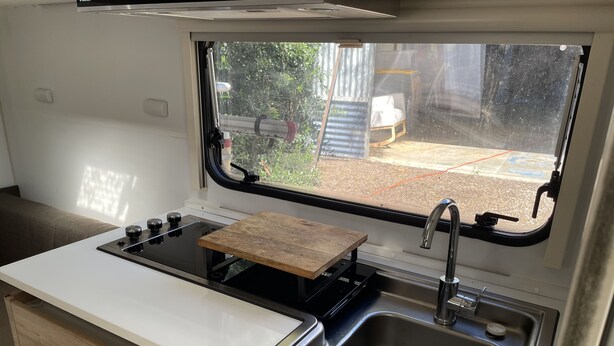 Una cocina compacta con estufa, lavamanos y ventana con vistas a un patio trasero.