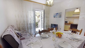 A dining area with a table set for four, a sofa, and a kitchen in the background. - Holiday apartment with three bedrooms, terrace, air conditioning and car park (Umag)