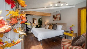 Ein Schlafzimmer mit einem Bett, einem Nachttisch, einem Sessel, einem Schreibtisch und einer Treppe, die zu einem anderen Raum führt.