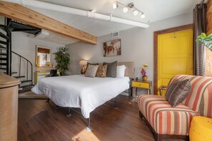 Une chambre à coucher avec un lit, un canapé, une petite table, un miroir, une plante et une porte jaune.