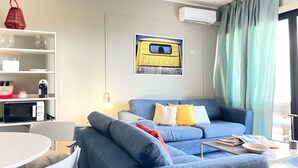 Ett modernt vardagsrum med en blå soffa, ett matbord och en köksdel med mikrovågsugn.
