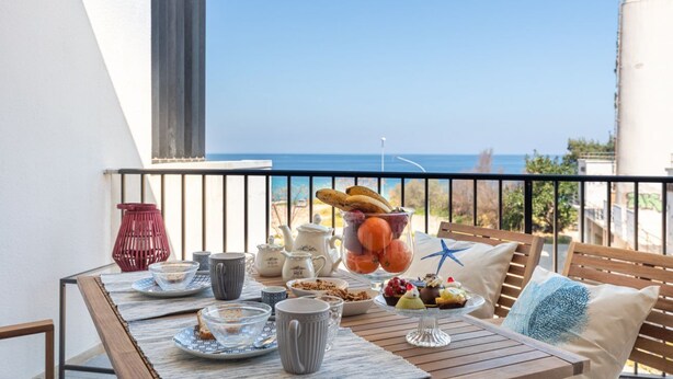 En balkong med ett bord dukat för frukost, med utsikt över havet.
