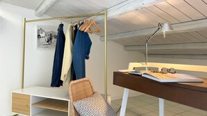 Ett sovrum med en säng, ett skrivbord med en lampa, en stol och en garderob med kläder hängande i.