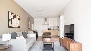 A modern living room with a sofa, coffee table, TV, and kitchen in the background.
