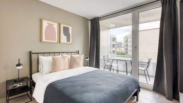 A modern bedroom with a bed, bedside table, and a view of the balcony.