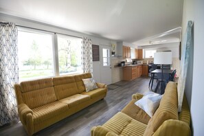 Un salon moderne comprenant un canapé, un coin repas avec une table et des chaises, et un espace cuisine avec des placards et des appareils électroménagers.