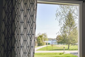 Une fenêtre ornée d’un motif géométrique, donnant sur une rue résidentielle, avec des maisons et un arbre visibles.