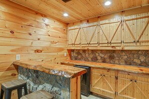 A wooden cabin interior with a stone accent wall, wooden cabinets, and a bar area.