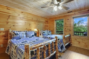 A wooden cabin bedroom with two beds, a ceiling fan, and large windows.