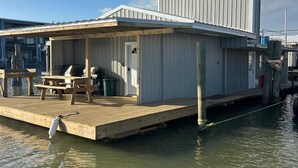 A docked house with a wooden deck and a small outdoor seating area. - Catfish house boat for rent, sleeps 8,Ice machine. perfect place to fish 🐠  (Venice)