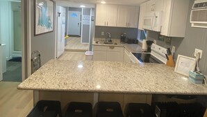 A modern kitchen with a granite countertop, white cabinets, and a built-in microwave. There are four black bar stools and a small sink. - Catfish house boat for rent, sleeps 8,Ice machine. perfect place to fish 🐠  (Venice)