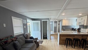 A modern living room with a grey sofa, a wooden floor, and a kitchen area with white cabinets and a countertop. - Catfish house boat for rent, sleeps 8,Ice machine. perfect place to fish 🐠  (Venice)