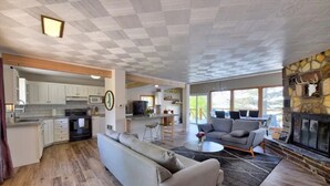 Amplia sala de estar con sofá, una mesa de centro y chimenea. Se ve una cocina con armarios blancos y un microondas al fondo.