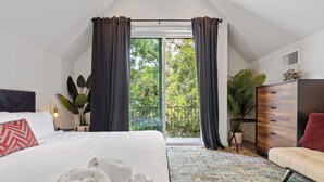 Habitación de hotel con una cama grande, un sofá, una ventana con cortinas, una planta en maceta y un mueble de madera.