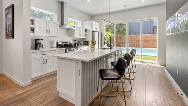 Una cocina moderna con armarios blancos, una isla grande y una zona de bar con sillas negras.