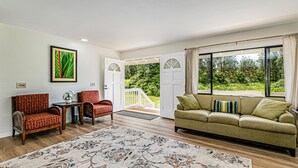 A spacious living room with a large window, a sofa, two armchairs, a coffee table, and a decorative rug.