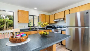 A modern kitchen with wooden cabinets, a granite countertop, stainless steel appliances, and a bowl of fruit.