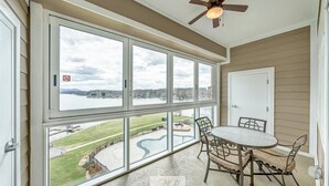 A room with large windows overlooking a body of water and a view of a park. There is a ceiling fan, a table with chairs, and a door. - #245 Pointe - 2 Bedroom Lakefront Condo at Mariners SML (Bedford County)