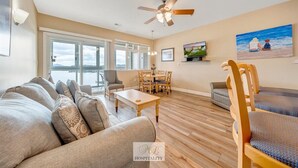 A spacious living room with a large sofa, a dining table, and a ceiling fan. - #245 Pointe - 2 Bedroom Lakefront Condo at Mariners SML (Bedford County)