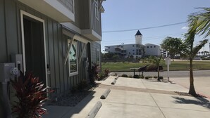 Il s’agit d’un bâtiment à l’architecture moderne, doté d’une grande fenêtre et d’une porte. Un trottoir s’étend devant le bâtiment, bordé d’un palmier et d’un banc.