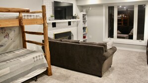 A cozy living room with a bunk bed, a fireplace, a sofa, and a large window. - Beautiful lakefront retreat, 4 bedroom, sleeps 8 (Huntsville)
