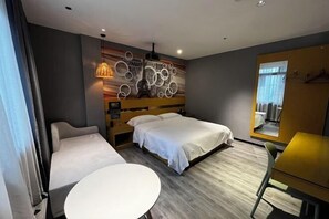 A hotel room with a bed, a sofa, a small table, a wall with circular patterns, and a window with curtains. - Tuke Boutique Hotel (Taishan)