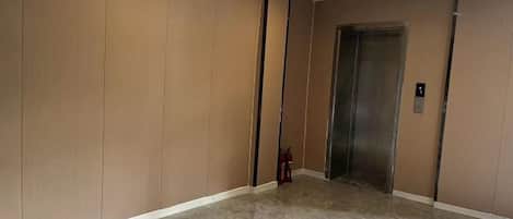 A hallway with a marble floor, a door, and an elevator.
