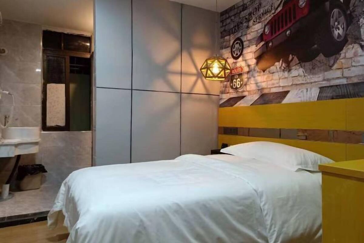 A bedroom with a bed, a wall-mounted light fixture, and a mural with a car and route number.