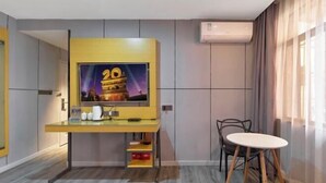 Ein modernes Hotelzimmer mit Flachbildfernseher an der Wand, einem kleinen Schreibtisch mit Stuhl und einem runden Tisch.