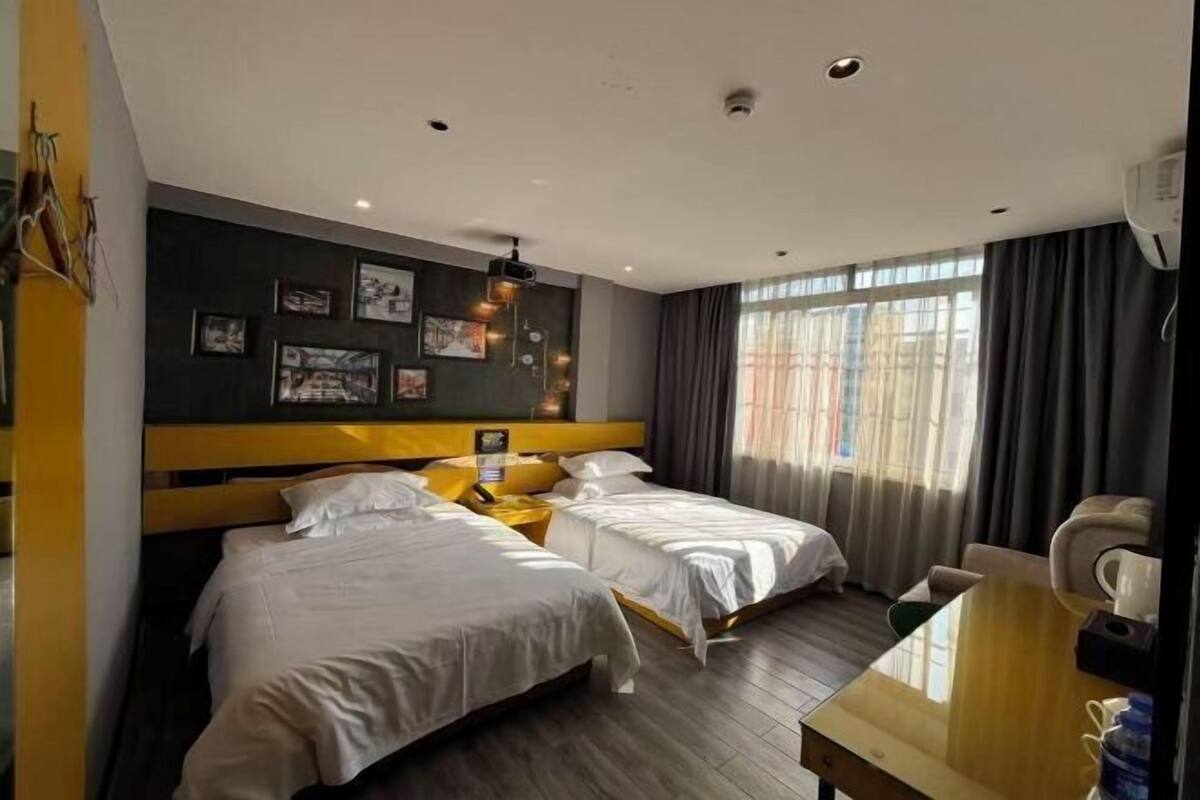 A hotel room with two beds, a desk, a chair, and a large window with curtains.