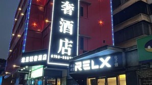 Ein Hotel mit beleuchteter Beschilderung, darunter ein auffälliges vertikales Schild mit chinesischen Schriftzeichen und ein horizontales Schild mit dem Wort „RELX“.