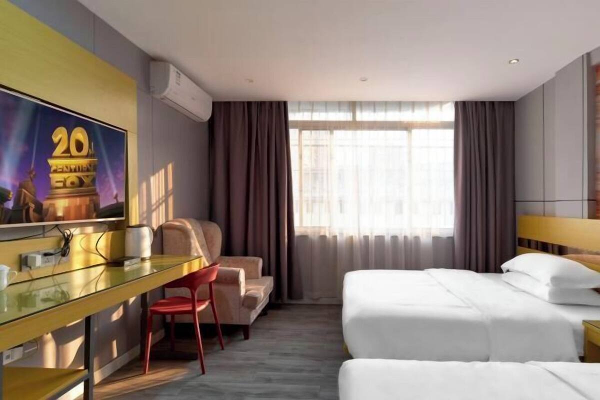 A hotel room with a bed, a desk, a chair, and a large window with curtains.