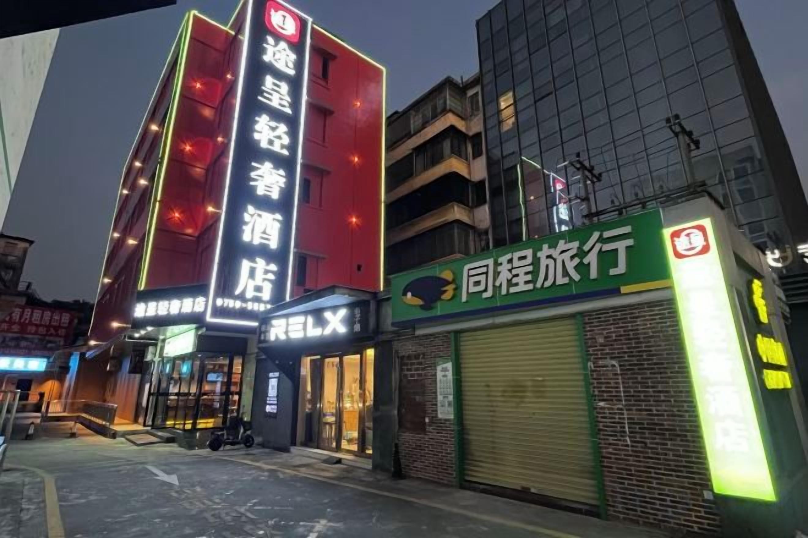 Un hotel con un letrero llamativo, una tienda cerrada con un letrero verde, y un edificio con fachada roja.