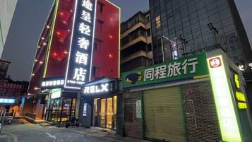 Un hotel con un letrero llamativo, una tienda cerrada con un letrero verde, y un edificio con fachada roja.