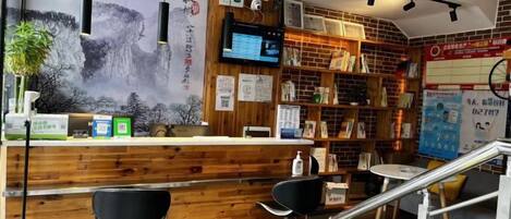 Un espace d’accueil avec un comptoir en bois, des chaises noires, un écran de télévision et un mur orné d’une fresque.