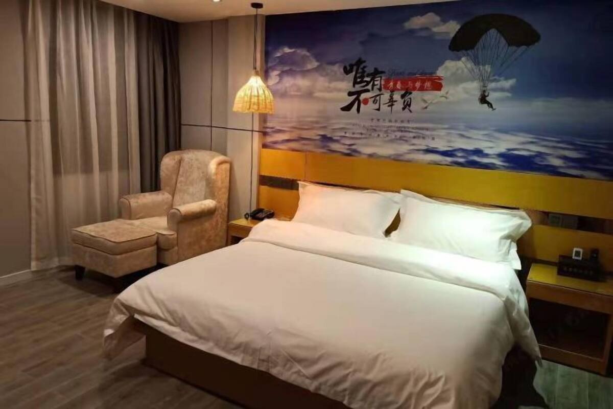 A hotel room with a bed, a chair, a nightstand, and a wall with a parachuting illustration.