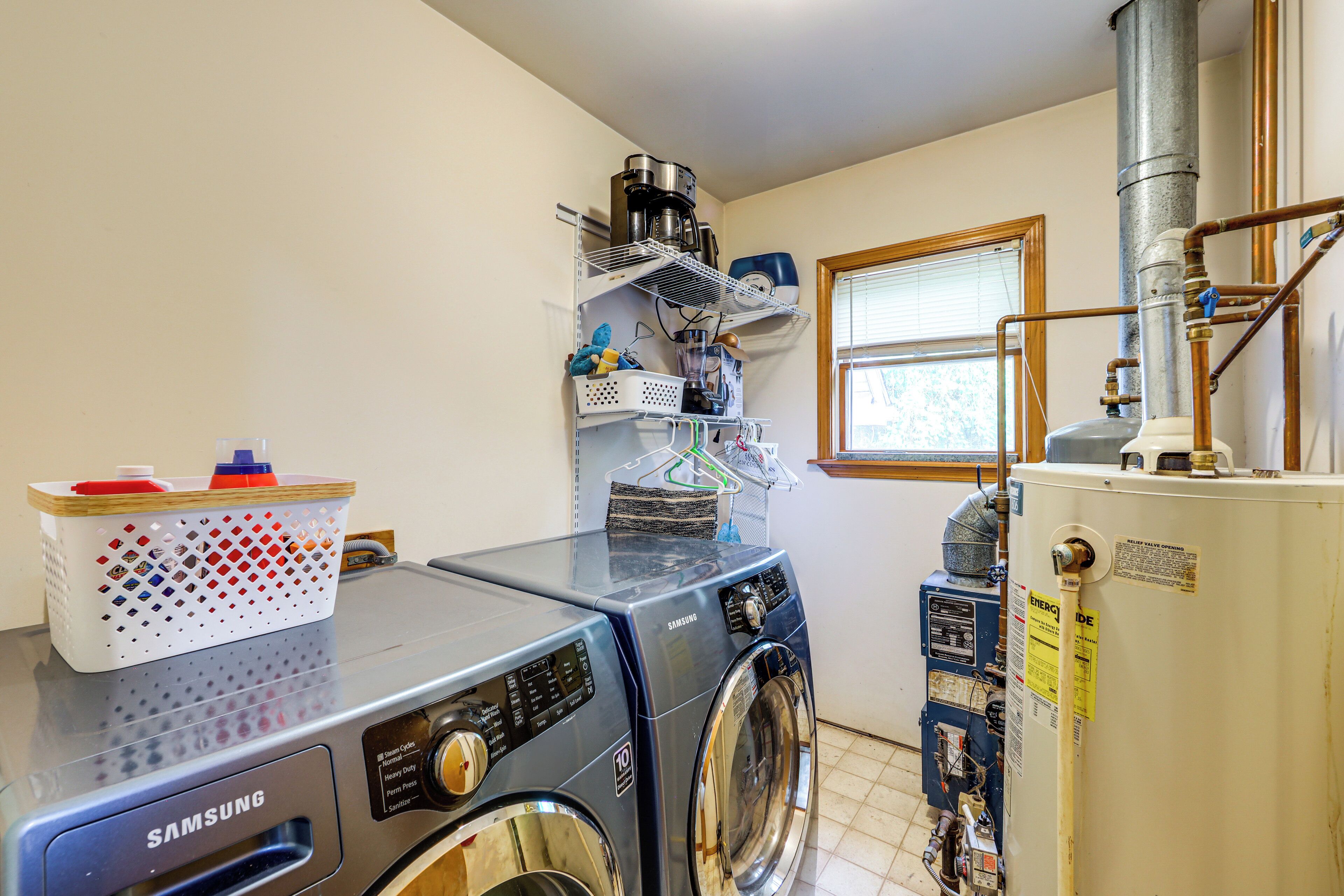 A laundry area with a Samsung washer and dryer, a water heater, and a window with blinds.